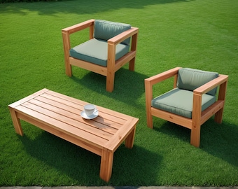 May include: Outdoor wooden furniture set on green grass. The set includes a rectangular coffee table and two armchairs with green cushions. A white teacup and saucer sit on the table.