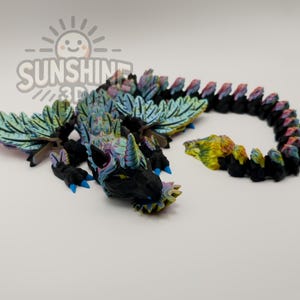 Puede incluir: Un juguete de dragón articulado impreso en 3D en negro, azul, verde y amarillo. El dragón tiene alas grandes y detalladas y un cuerpo segmentado. El texto "SUNSHINE 3D" está en la esquina superior izquierda.