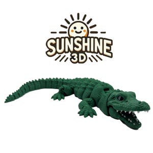 Puede incluir: Un juguete de cocodrilo verde impreso en 3D con escamas detalladas y mandíbulas abiertas. El juguete está tumbado y tiene una superficie texturizada. La imagen incluye el texto "SUNSHINE 3D" con un logotipo de sol.