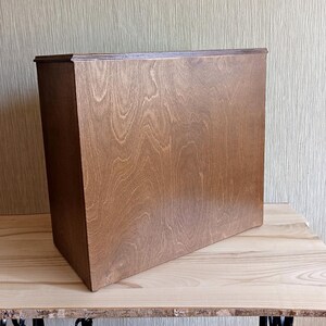 May include: A rectangular wooden box with a rich brown finish, showcasing the natural wood grain. The box is placed on a light-colored wooden surface, with a textured wall in the background. The box appears to be a storage container or decorative item.