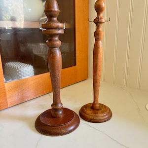 May include: Two wooden hat stands with metal hooks. The stands are brown and have a round base.