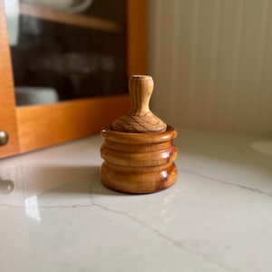 Pode incluir: Um conjunto de saleiro e pimenteiro de madeira com base redonda e topo cilíndrico. O saleiro tem um acabamento de madeira natural e é feito de várias camadas de madeira.