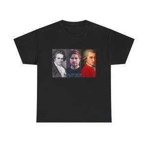 Puede incluir: Camiseta negra con un diseño rectangular que muestra tres retratos. Los retratos muestran a un hombre con traje, un hombre con camisa oscura y un hombre con abrigo rojo. La camiseta está hecha de tela oscura.