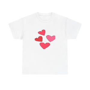 May include: White t-shirt featuring a design of four hearts in shades of red and pink. The hearts are arranged in a cluster, with a simple, hand-drawn style. The shirt is made of a soft, comfortable material.