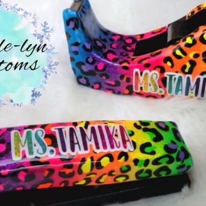 May include: A colorful desk set featuring a tape dispenser and stapler, both adorned with a vibrant leopard print in shades of blue, purple, pink, orange, and green. The name "MS. TAMIKA" is displayed on each item.