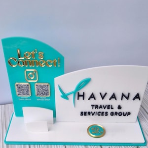May include: A teal and white acrylic display stand featuring the text Let's Connect! in gold, two QR codes, and the Havana Travel & Services Group logo in black. The stand includes a small white card holder and a circular gold NFC contact icon.