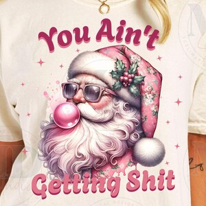 May include: A white t-shirt with a pink and white illustration of Santa Claus wearing sunglasses and blowing a pink bubble. The text "You Ain't Getting Shit" is printed in pink below the illustration.