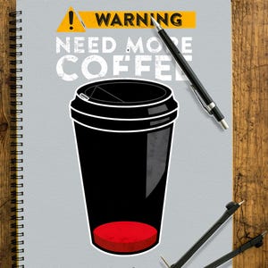 Könnte beinhalten: Ein Notizbuch mit grauem Einband, das eine schwarze Kaffeetasse mit rotem Boden zeigt. Der Text lautet "WARNING NEED MORE COFFEE". Ein schwarzer Stift, ein Zirkel und Schreibwaren liegen auf einer Holzoberfläche.