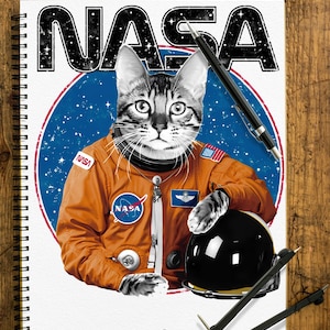May include: A black and white cat wearing an orange spacesuit with a NASA logo on the chest. The cat is holding a black helmet in its right paw. The background is a blue circle with white stars and the word "NASA" in black letters.