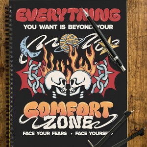 Può includere: Quaderno nero a spirale con la scritta "EVERYTHING YOU WANT IS BEYOND YOUR COMFORT ZONE". Il design include teschi, fiamme ed elementi celesti. Una penna e un compasso sono su una superficie di legno.