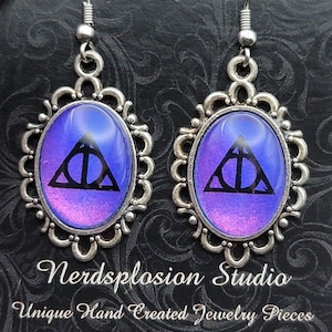 Peut inclure: Boucles d'oreilles argentées avec un pendentif ovale orné d'un symbole des Reliques de la Mort noir sur fond bleu et violet. De Nerdsplosion Studio, Unique Hand Created Jewelry Pieces.