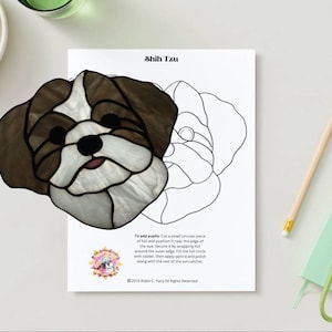 Puede incluir: Un atrapasoles de perro Shih Tzu de vidrieras. La cabeza del perro es marrón, blanca y negra con una lengua rosa. Un dibujo lineal de la cabeza del perro está en una hoja de papel blanca. El texto "Shih Tzu" está en la parte superior.