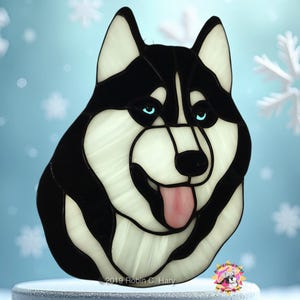 May include: Stained glass art of a black and white husky dog with blue eyes. The dog is looking to the right and has its tongue sticking out. The background is a light blue color with snowflakes.