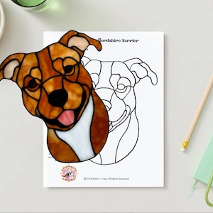 Puede incluir: Un perro Staffordshire Terrier de vidriera con detalles marrones, blancos y negros. El perro sonríe con la lengua fuera. Un contorno en blanco y negro del perro está sobre un papel blanco. Las palabras "Yorkshire Terrier" están en la parte superior del papel.
