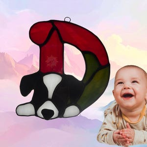 Alphabet letter-D- shown with a puppy. Letter is made of red and green glass while the puppy is made of black and white glass. Puppy represents December.
