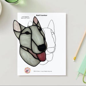 May include: A stained glass pattern of a Bull Terrier dog's head, with a white and gray color scheme, black nose, and red tongue. The design is labeled "Level: Beginner" and measures 5.2" x 8".