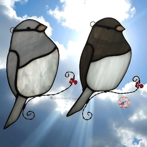 May include: Two stained glass bird ornaments perched on a wire branch with red berries. One bird is gray and white, the other is brown and white. The background is a blue sky with clouds.