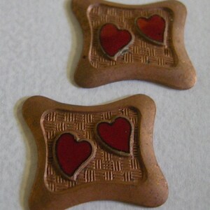 May include: Two small, brown, heart-shaped metal charms with a woven pattern and red enamel hearts.