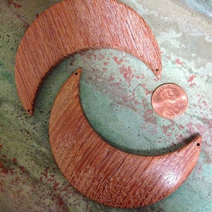 May include: Two wooden crescent moon shapes, one on top of the other, with a brown wood grain pattern. The moons are unfinished and have a natural wood color.