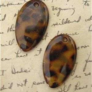 May include: Two brown and black oval-shaped tortoise shell resin buttons with a hole in the top.