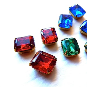 May include: Assortment of colorful glass gems with gold settings. The gems are red, green, and blue.