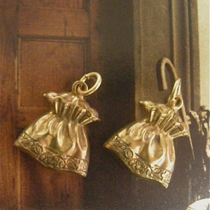 May include: A pair of gold-tone earrings shaped like small bags with a detailed design. The earrings have a hook closure.