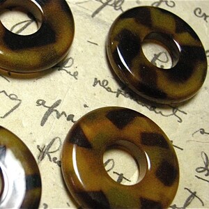 May include: Four brown and black patterned round plastic or resin beads with a hole in the center. The beads are approximately 1 inch in diameter.