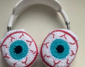 May include: White headphones with crocheted eye covers. The eye covers are white with red veins and a blue iris with a black pupil.