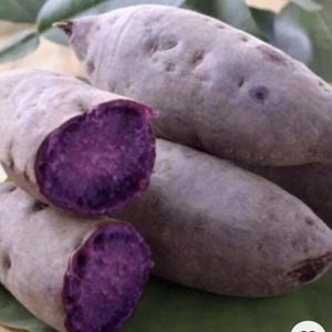 May include: Several purple sweet potatoes, with a few cut open to reveal the vibrant purple flesh. The potatoes have a light brown skin and are arranged on a green leaf. The image highlights the contrast between the exterior and interior colors.