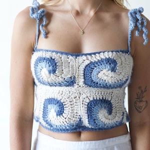 Könnte beinhalten: Handgehäkeltes Crop-Top mit blau-weißem Wellenmuster. Das Oberteil hat Bindeträger und einen quadratischen Ausschnitt. Das Kleidungsstück ist im Crop-Top-Stil gehalten.