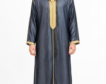 Könnte beinhalten: Eine dunkelblaue Djellaba mit Kapuze und langen Ärmeln, verziert mit goldener Stickerei entlang der vorderen Knopfleiste, den Ärmelbündchen und dem Kapuzenrand. Das Kleidungsstück ist bodenlang, gerade geschnitten und wird über einer weißen Hose getragen.