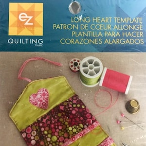 May include: A green and pink fabric heart-shaped sewing kit with the text "LONG HEART TEMPLATE PATRON DE COEUR ALLONGE PLANTILLA PARA HACER CORAZONES ALARGADOS" on the packaging.