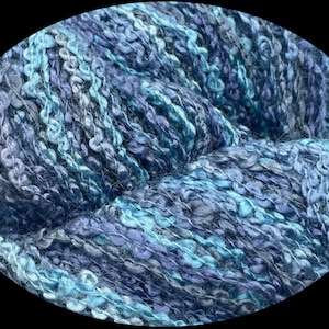 May include: A close-up of a blue and teal yarn with a textured, fuzzy appearance. The yarn is made of a blend of fibers, creating a unique and interesting look.