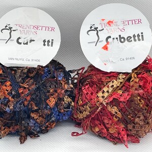 May include: Two balls of yarn, one brown, red, and gold, and the other blue, brown, and orange. Both balls have a white label with the text "TRENDSETTER YARNS" and "Cubetti" or "Curtti" and the address "VAN NUYS, Ca. 91406".