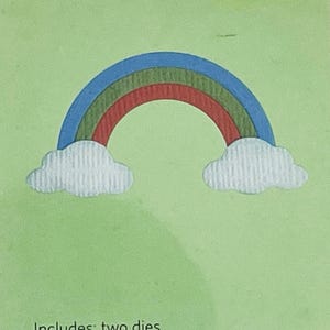 May include: A colorful rainbow die-cut design with blue, green, and red arches, and two white cloud shapes. The design is set against a light green background. The text "Includes: two dies" is at the bottom.