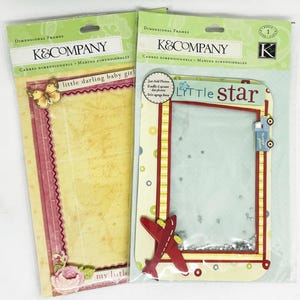 May include: Two dimensional frames for baby photos. One frame has a butterfly and the text "little darling baby girl". The other frame has a red airplane and the text "little star". Both frames have a clear plastic window.