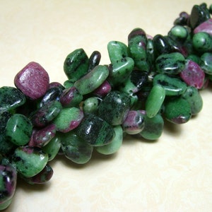 May include: A strand of green and pink gemstone beads, tumbled into a smooth, pebble shape. The beads are a mix of green, pink, and black.