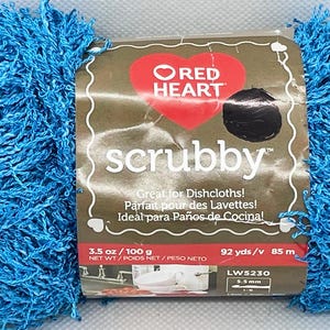 Pode incluir: Um novelo de fio "scrubby" azul brilhante com um r&oacute;tulo com um logotipo de cora&ccedil;&atilde;o vermelho e a palavra "scrubby". O r&oacute;tulo inclui texto em ingl&ecirc;s, franc&ecirc;s e espanhol. O fio pesa 100 g e mede 85 m.