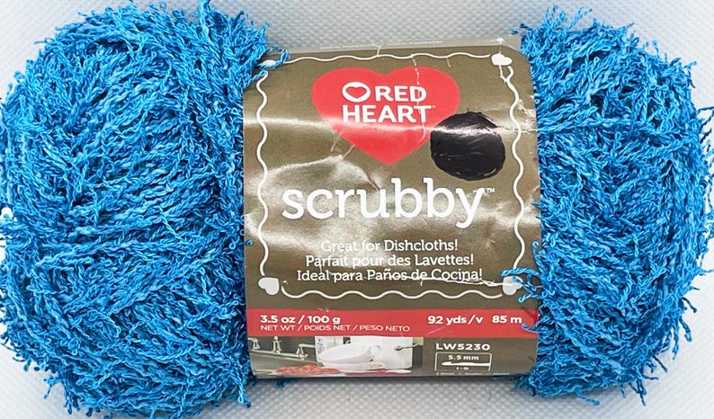 Pode incluir: Um novelo de fio "scrubby" azul brilhante com um r&oacute;tulo com um logotipo de cora&ccedil;&atilde;o vermelho e a palavra "scrubby". O r&oacute;tulo inclui texto em ingl&ecirc;s, franc&ecirc;s e espanhol. O fio pesa 100 g e mede 85 m.