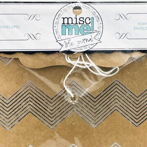 May include: A package of kraft paper envelopes with a chevron design. The package is sealed in clear plastic and includes a label with the text "misc me! life journal". The envelopes are tied together with white string.