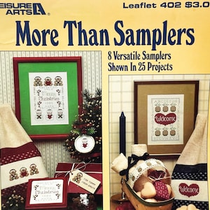 May include: A Leisure Arts craft leaflet titled More Than Samplers, 8 Versatile Samplers Shown In 25 Projects, featuring cross-stitch designs of teddy bears, pineapples, and holiday themes displayed in frames, on fabric, and on gift tags.