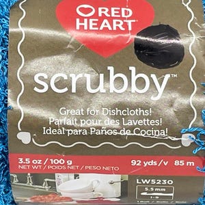 Pode incluir: Um close-up de uma bola de fio azul scrubby. A etiqueta diz "Red Heart scrubby" e inclui texto em ingl&ecirc;s, franc&ecirc;s e espanhol. O fio tem 100 g e 85 m.