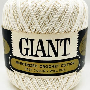 May include: A ball of off-white mercerized crochet cotton yarn wrapped in a black and gold paper label. The label features the text GIANT in large black letters, followed by MERCERIZED CROCHET COTTON, FAST COLOR, and WILL BOIL in black text.