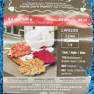 Pode incluir: Um pacote de fio azul com um r&oacute;tulo mostrando panos de prato de croch&ecirc; coloridos. O r&oacute;tulo inclui o texto "Great for Dishcloths!" e medidas de 100 g e 85 m.