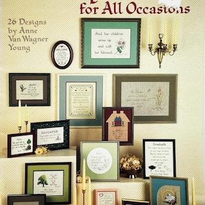 May include: A collection of framed cross-stitch designs with various scriptures and quotes. The frames are in different shapes and colors, including green, brown, and blue. The image also includes candles and a book, suggesting a religious or inspirational theme.