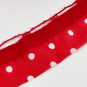 May include: Red fabric trim with white polka dots and a fringed edge.