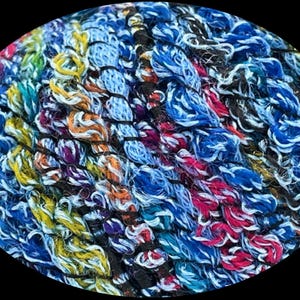 May include: Close-up of a skein of colorful yarn with a mix of blue, white, yellow, orange, red, and black threads. The yarn has a fuzzy texture and is perfect for crocheting or knitting.