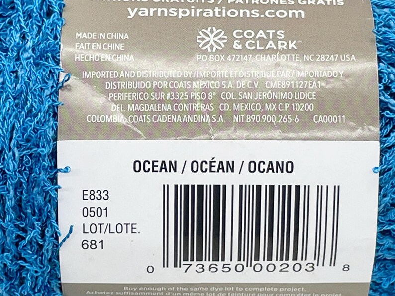 Pode incluir: Uma etiqueta de fio azul, com a palavra "OCEAN" e um c&oacute;digo de barras. A etiqueta tamb&eacute;m inclui a marca "COATS & CLARK" e o site "yarnspirations.com".