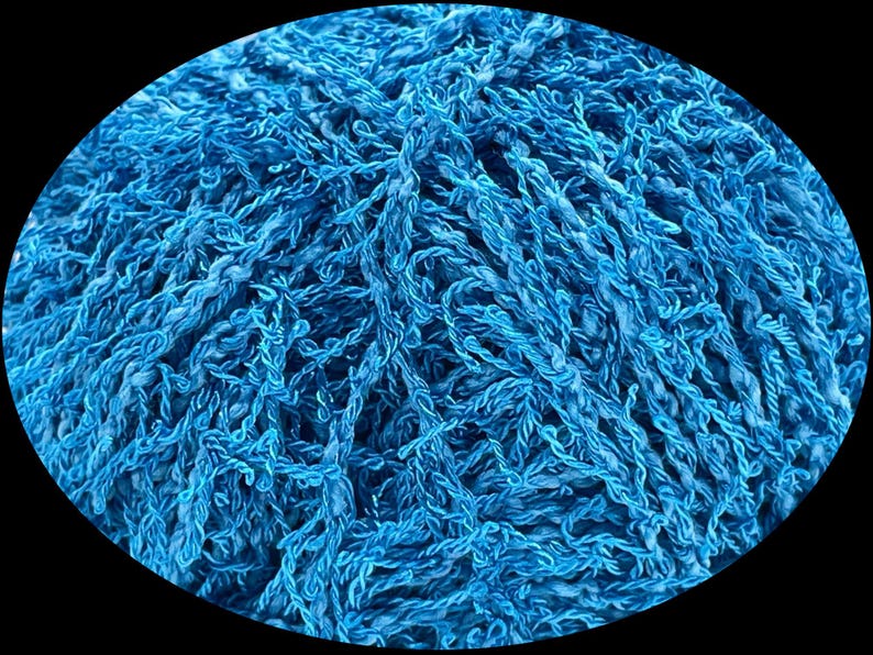 Pode incluir: Close-up de uma bola de fio azul brilhante. O fio parece ser uma fibra texturizada e torcida, possivelmente algod&atilde;o ou l&atilde;, com uma apar&ecirc;ncia ligeiramente difusa. A imagem est&aacute; em um fundo preto.