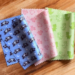 Peut inclure: Trois échantillons de tissu rectangulaires aux bords dentelés. L'échantillon bleu présente un motif répétitif de pandas, d'étoiles et de croissants de lune. L'échantillon rose affiche un motif de lapins. L'échantillon vert montre un motif de dinosaures.